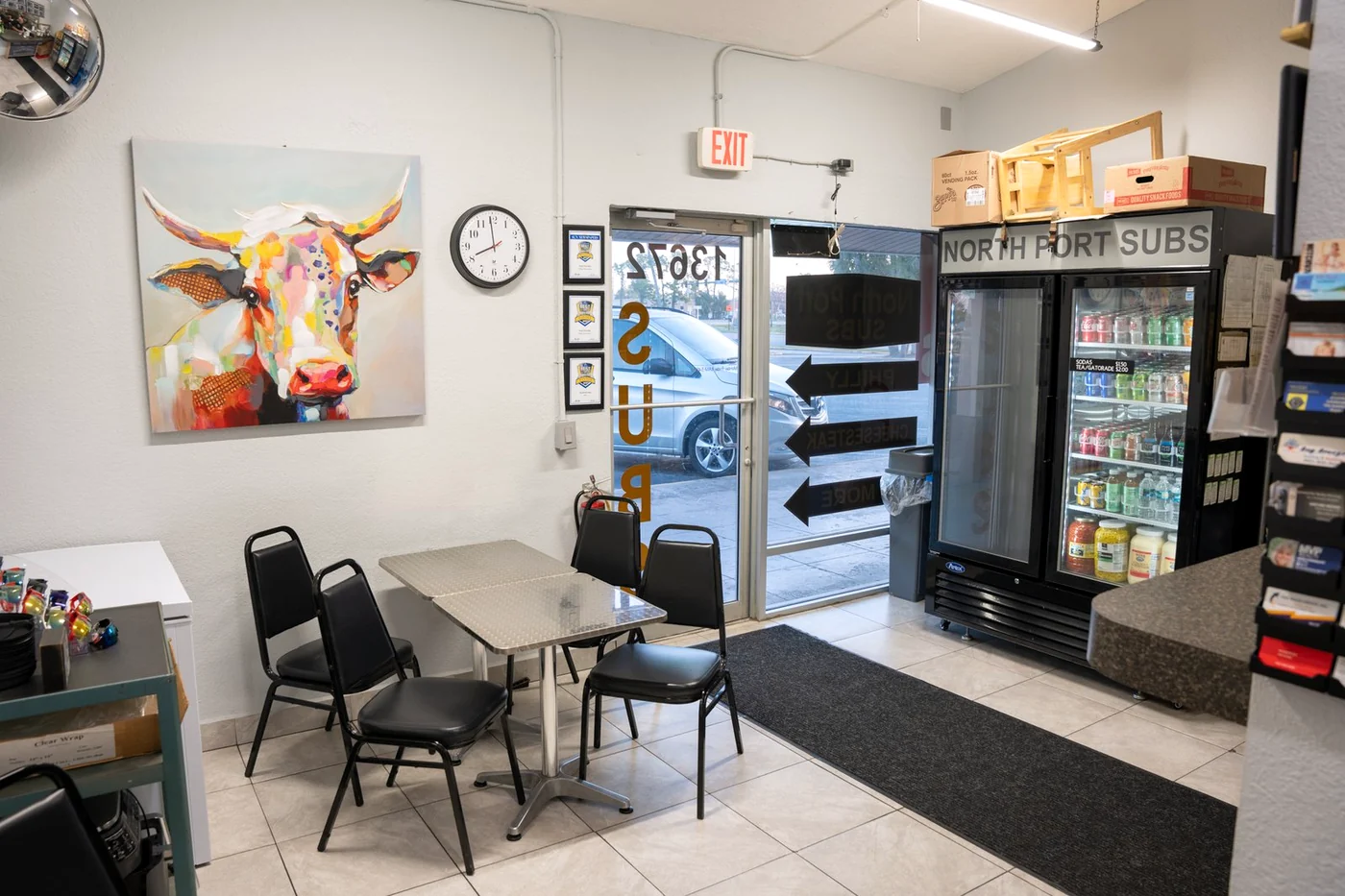 North Port Subs dining area with tables, colorful cow artwork and front entrance